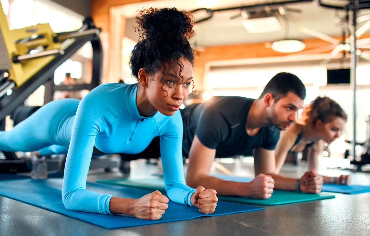 Two people doing planks on yoga mats in a bright room.